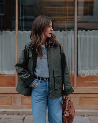 Woman wears green barn coat, grey knit, blue jeans