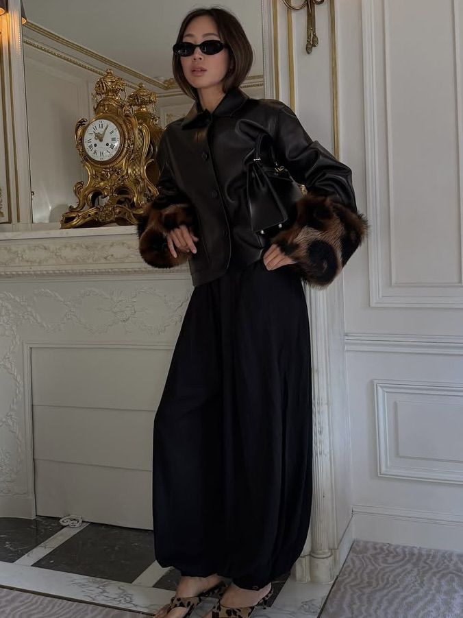Aimee Song wearing black trousers and a black leather jacket with animal-print fur cuffs.