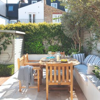 wooden dining table and chairs in small garden with white rendered raised beds and paving stones