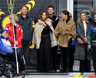 Prince Harry, Michael Buble and his wife, and Meghan Markle watching a curling competition as Buble adjusts his wife's coat