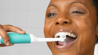 A woman brushing her teeth with an electric toothbrush