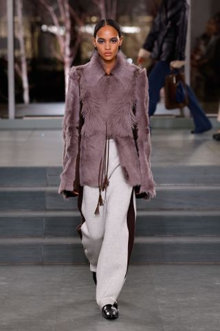 Tory Burch model walking the fall 2025 runway in a fur coat and track pants