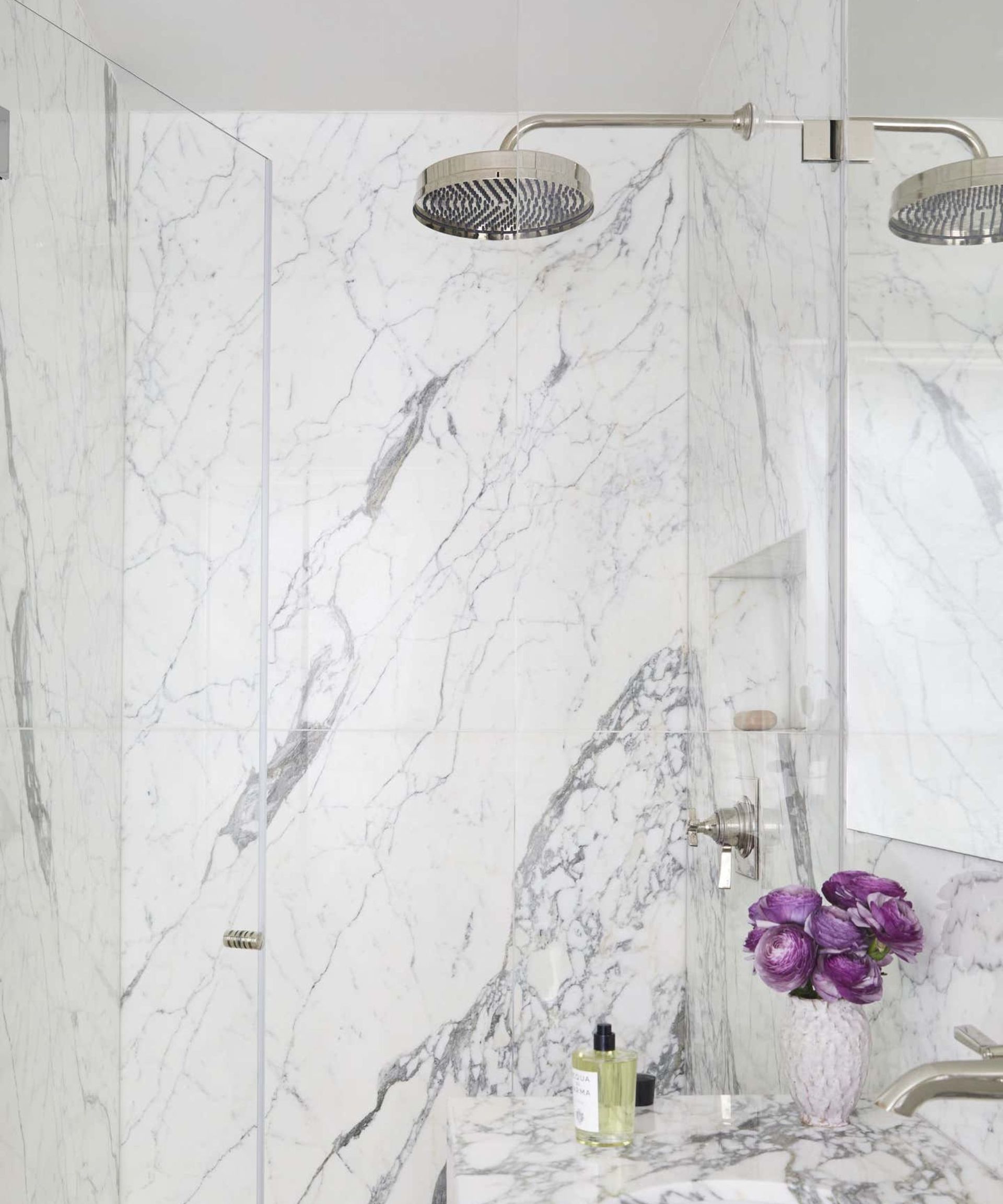 An oversized showerhead in a marble shower