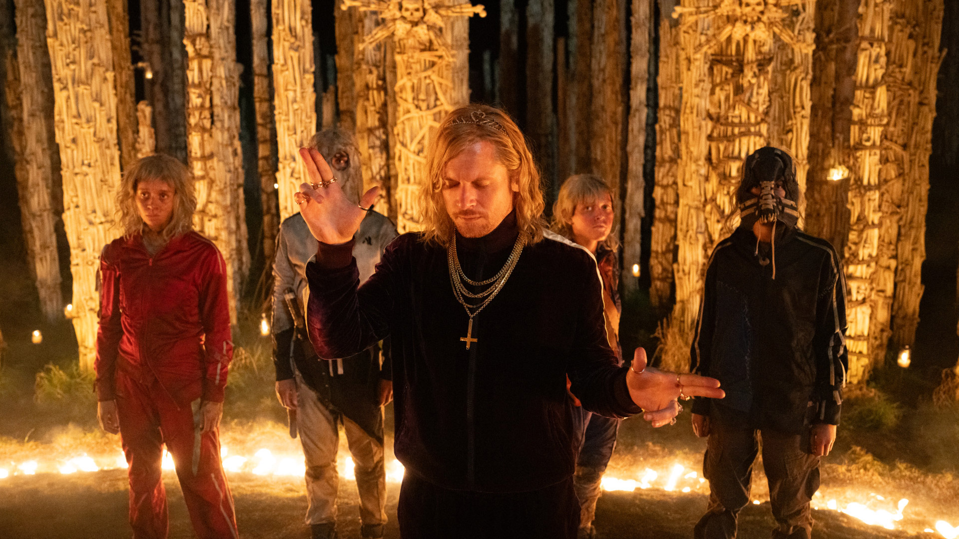 Jack O'Connell points finger guns surrounded by a cultist group wearing tracksuits in 28 Years Later: The Bone Temple
