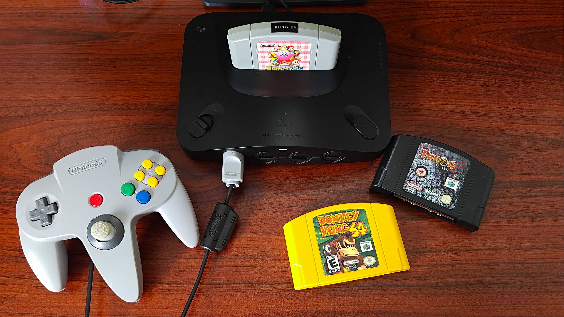 Analogue 3D with Kirby 64 cartirdge inserted next to original controller, Donkey Kong 64 yellow cartridge, and black Turok 2 cart.