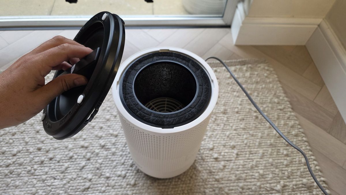A man's hand removes the bottom of the Coway Airmega 100, revealing the filter inside.