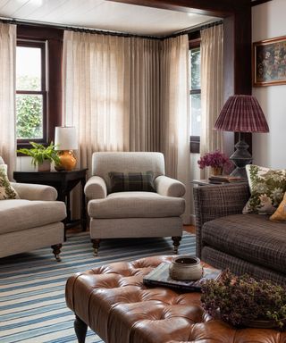Cozy living room with two cream armchairs, coffee table, gray sofa, table lamp, two windows with cream curtains