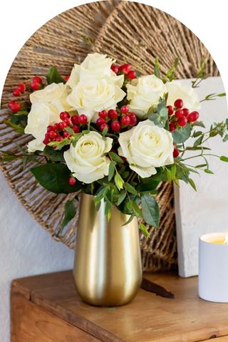 A bouquet of white roses and red berries in a gold vase.