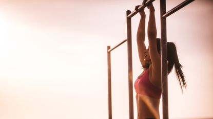 Young female fitness model doing pull ups at sunset next to the beach