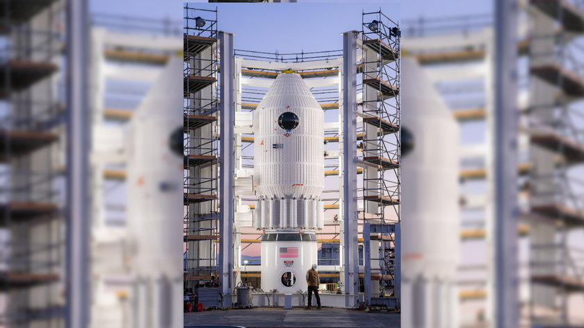 a white cylindrical vessel with conical top is mounted to stand on a test area, surrounded by railed scaffolding.