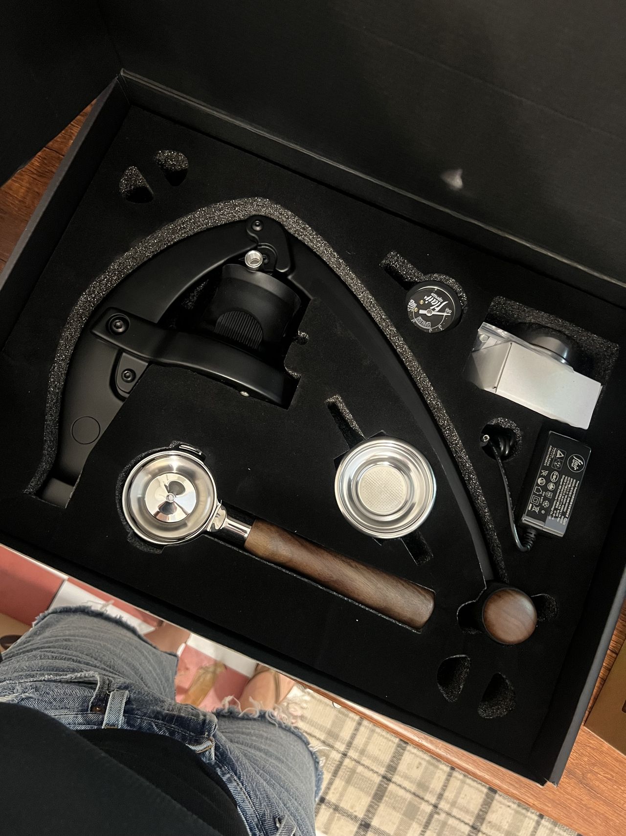 Image of a black box, open, showing a coffee machine and all of its accessories organized inside.