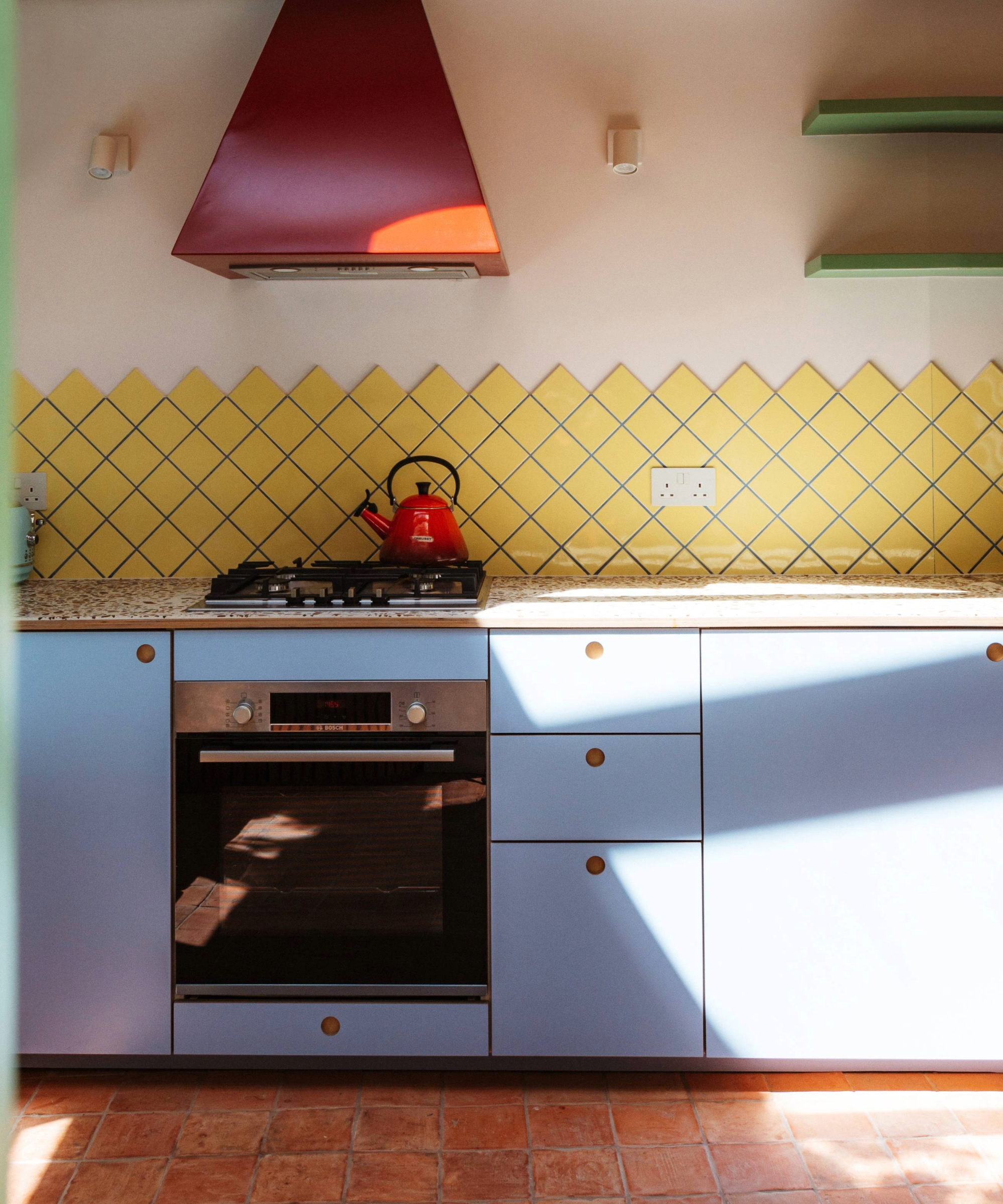 Kitchen with yellow splashback tiles and blue grout, lilac cabinets and red extractor fan