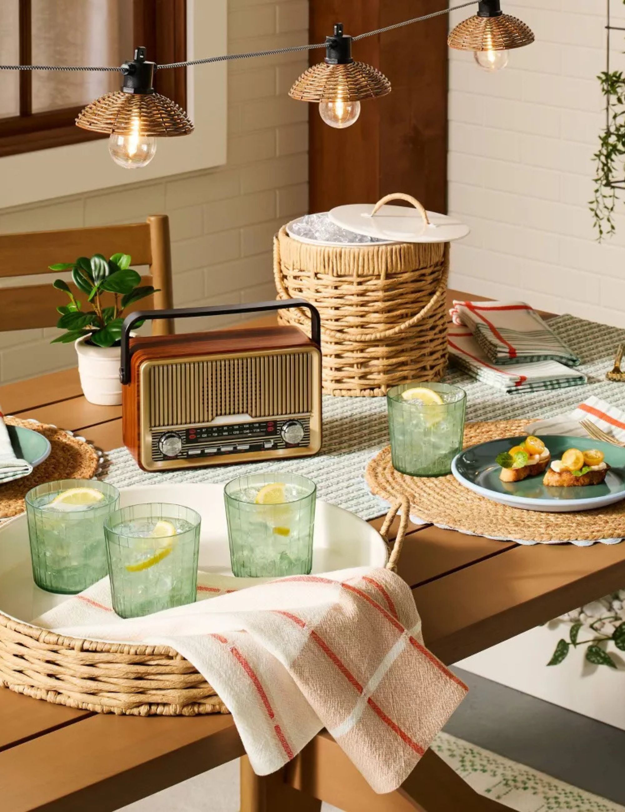 Outdoor table with rattan ice bucket and tray and drinks in green glass vases with an old fashioned radio