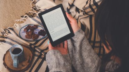 A woman reading an e-reader, while enjoying a coffee and cake