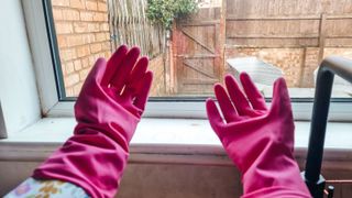 Two hands with pink rubber gloves on, against a window
