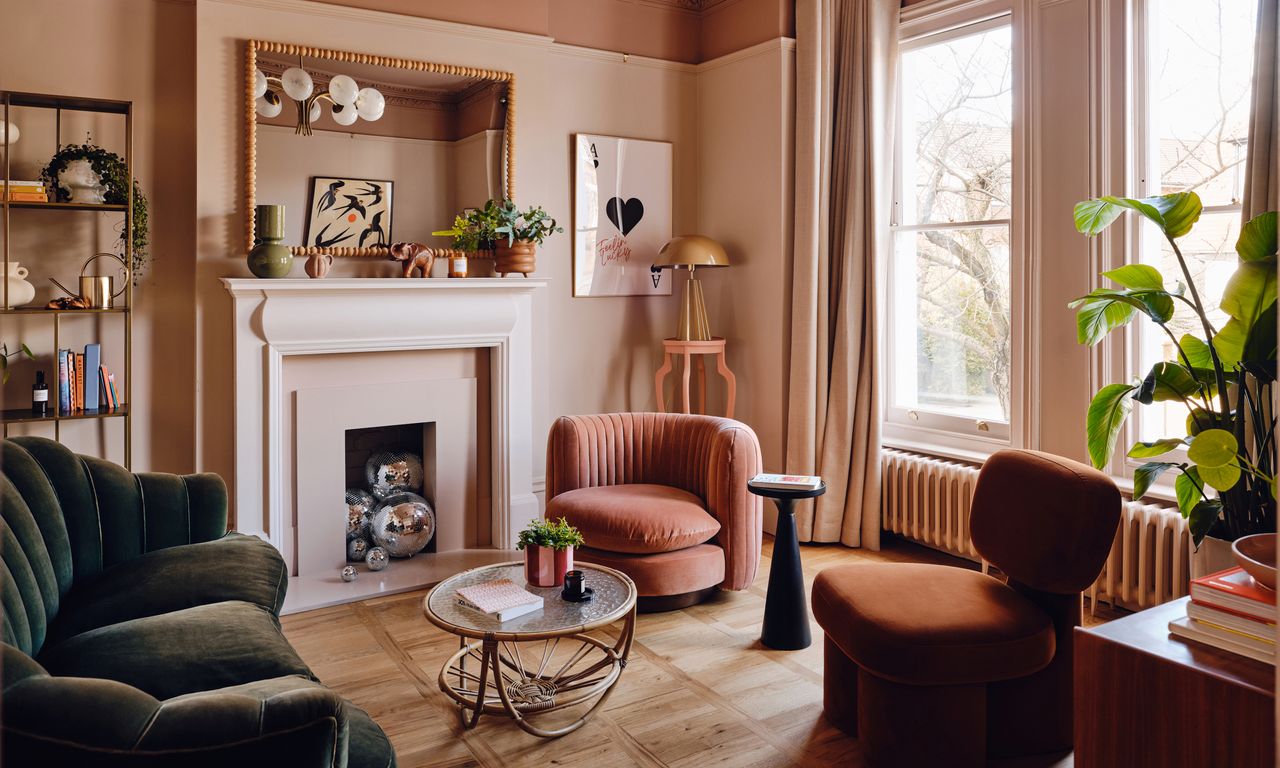 Pink living room with dark green sofa, coral and rust orange armchairs, bamboo and glass coffee table and bamboo mirror over white fireplace
