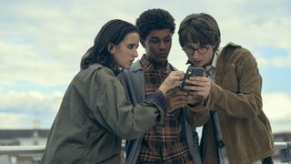 Ema, Mickey, and Arthur stare at a mobile phone in Harlan Coben's Shelter