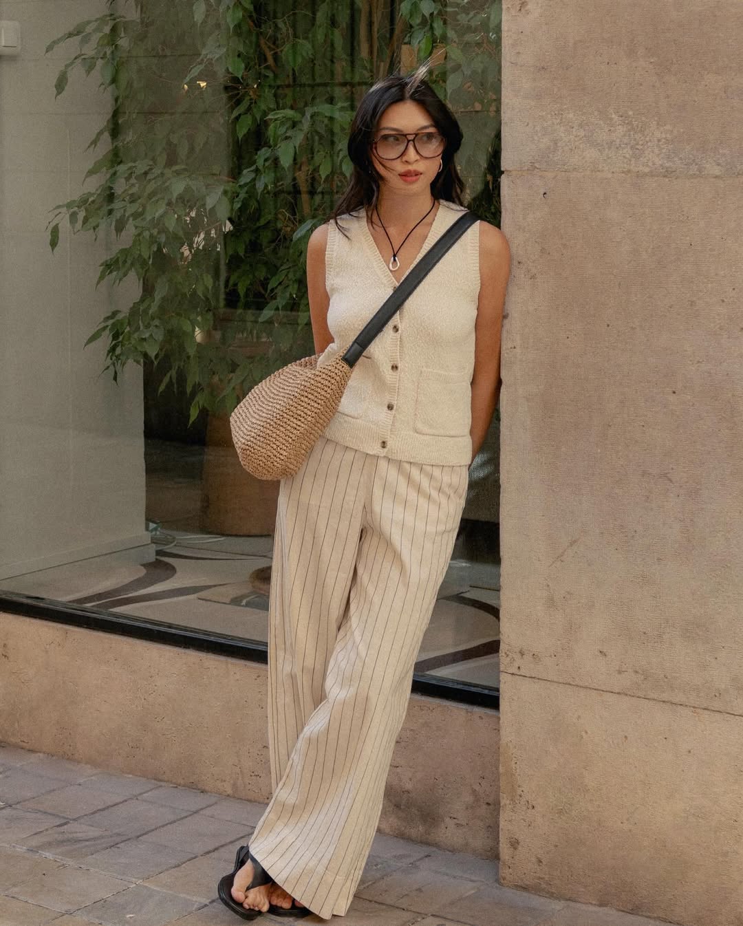 @michellelin.lin wears a cream knitted vest, striped linen trousers, black leather flip-flops and a raffia crossbody bag
