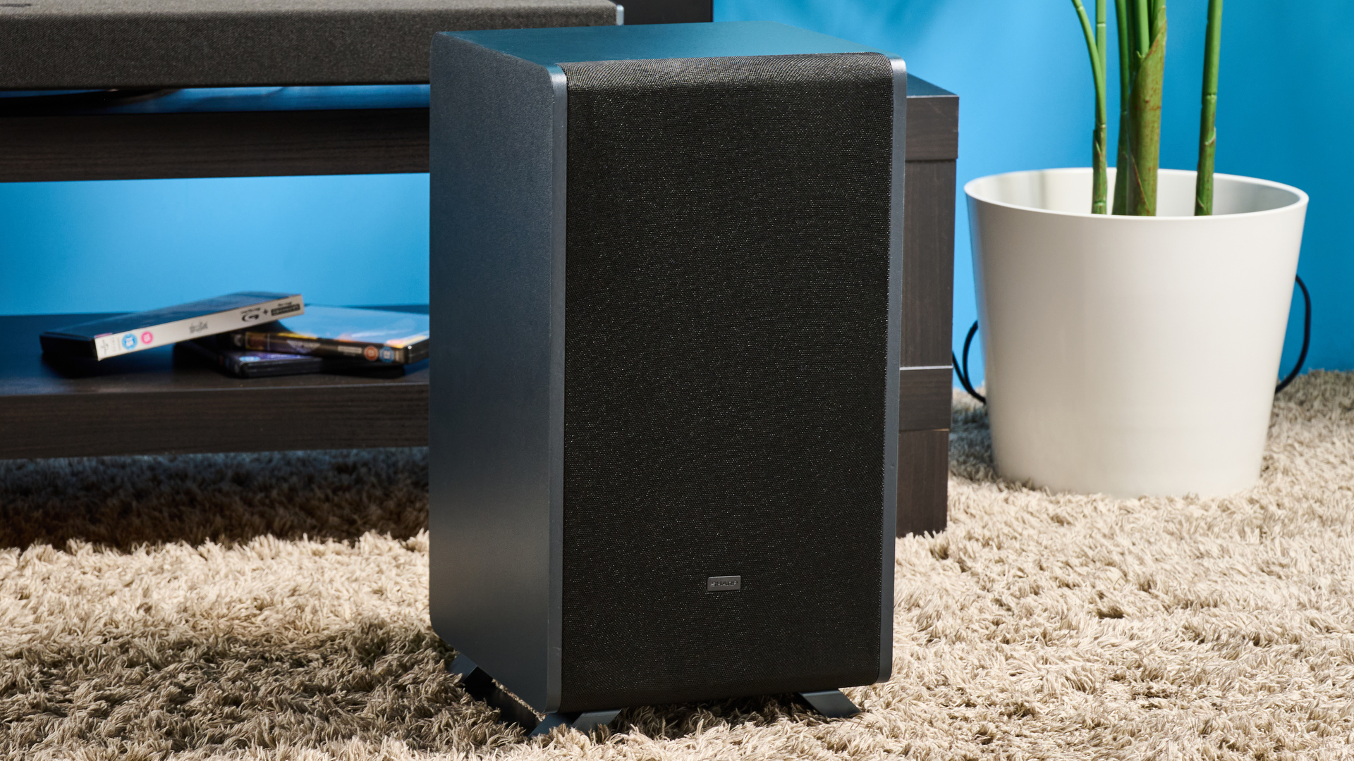 the Sharp 3.1.2 HT-SBW53121 Soundbar in black with a remote, subwoofer, against a blue background next to a panasonic TV