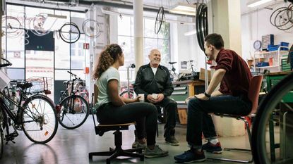 Photo of three people sitting on chairs facing each other in a bicycle shop