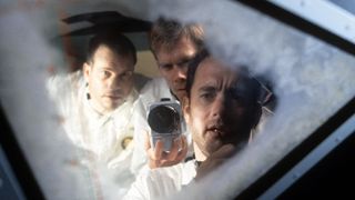 three men look through a frosted window. one holds a camera.