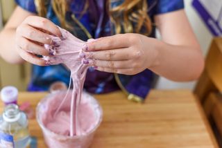 A close up of a young girl's hands holding and creating slime in a creative science experiment.