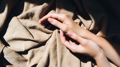 Two hands on beige sheet wearing glittering gel nail polish