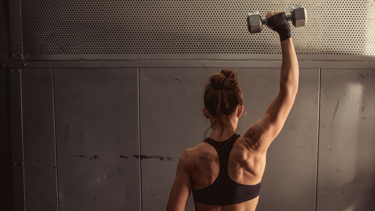 Woman performing shoulder press with one dumbbell