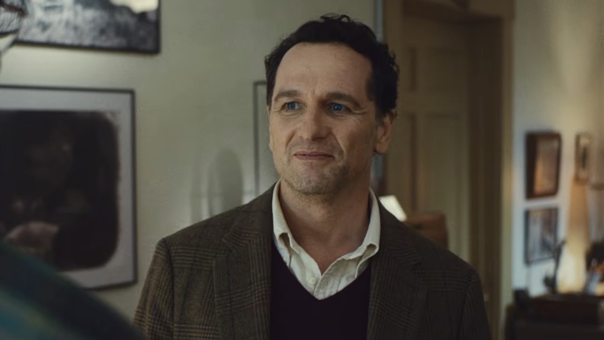 Matthew Rhys' Tom smiling in a blazer while trying to impress the New York Times journalist in Widow's Bay. 