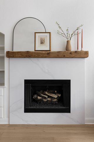 living room fireplace with beam mantel, mirror, candlesticks, faux florals and artwork