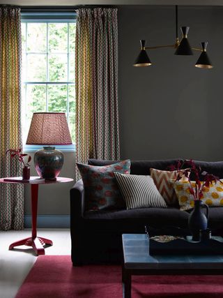 living room with gray walls and velvet couch, patterned cushions, red side table, black retro pendant, patterned cushions and lampshade