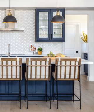 A kitchen with dark blue cabinetry and textured white backsplash tiles
