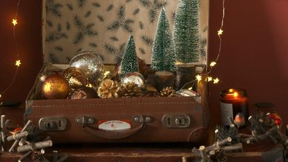 a cosy country living room with wood panel wallpaper, a roaring fire with a white mantle, a red armchair, a decorated christmas tree with presents underneath and a wreath and white star decorations on the wall