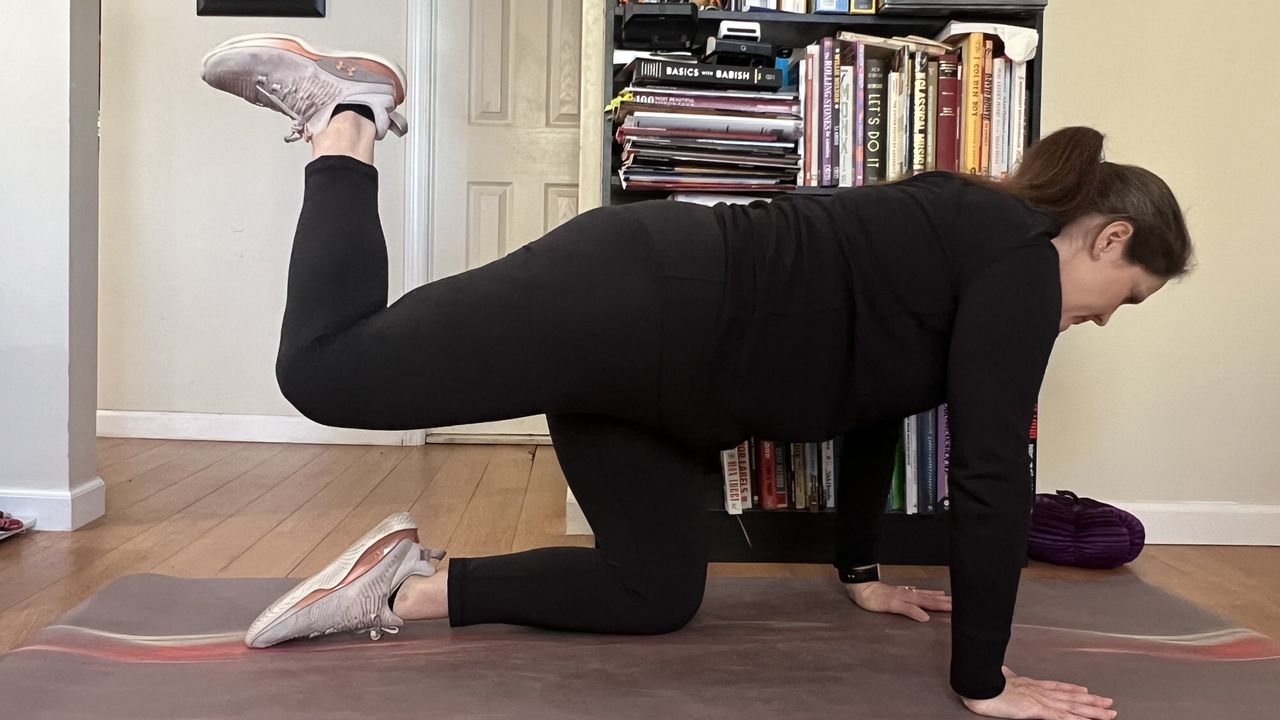 Jennifer RIzzuto demonstrates how to perform a hip CAR at home on a yoga mat in a living room. She is on all fours, with her leg bent and elevated behind her.