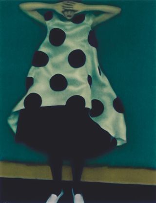 A model wearing a dress with big black spots posed against a green background