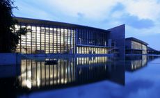 A modern building with steel and clear glass panel design. Photographed at dusk by a still river 