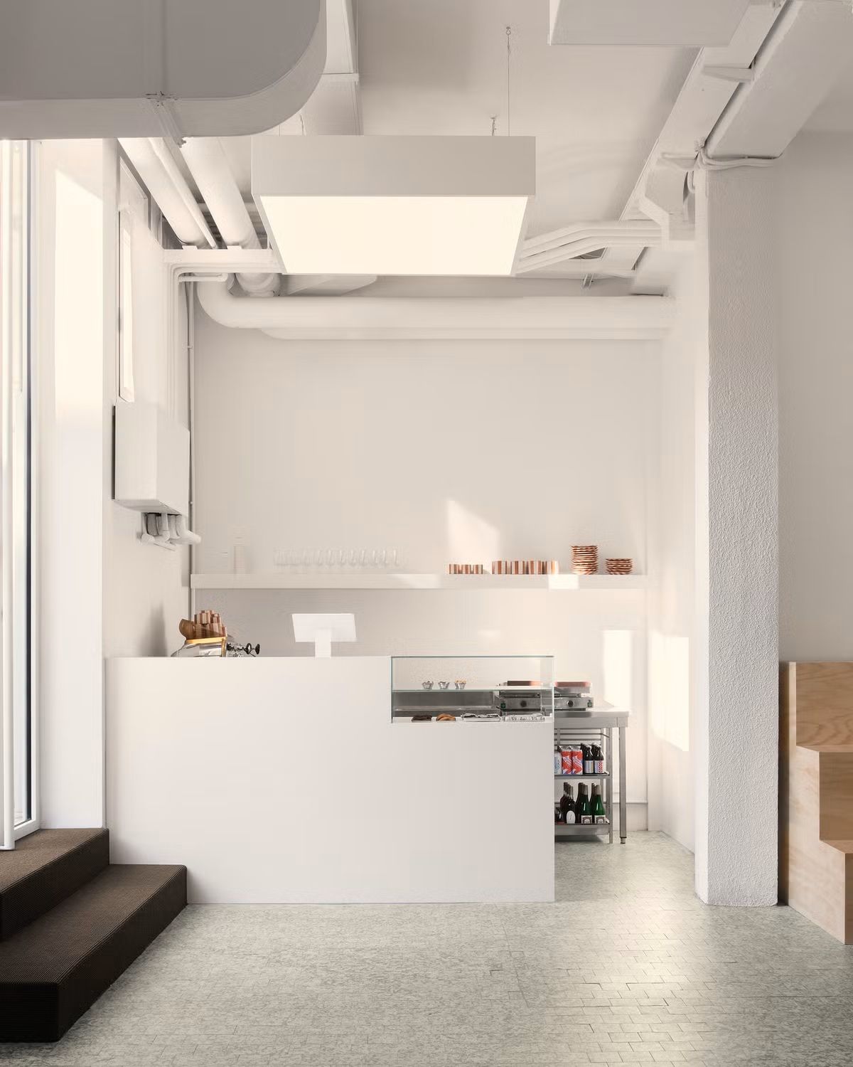 A hyper-minimalist, industrial-style cafe features white walls, chrome details, and pastries on show.