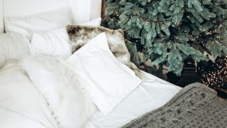 bed with white and grey pillows by Christmas tree