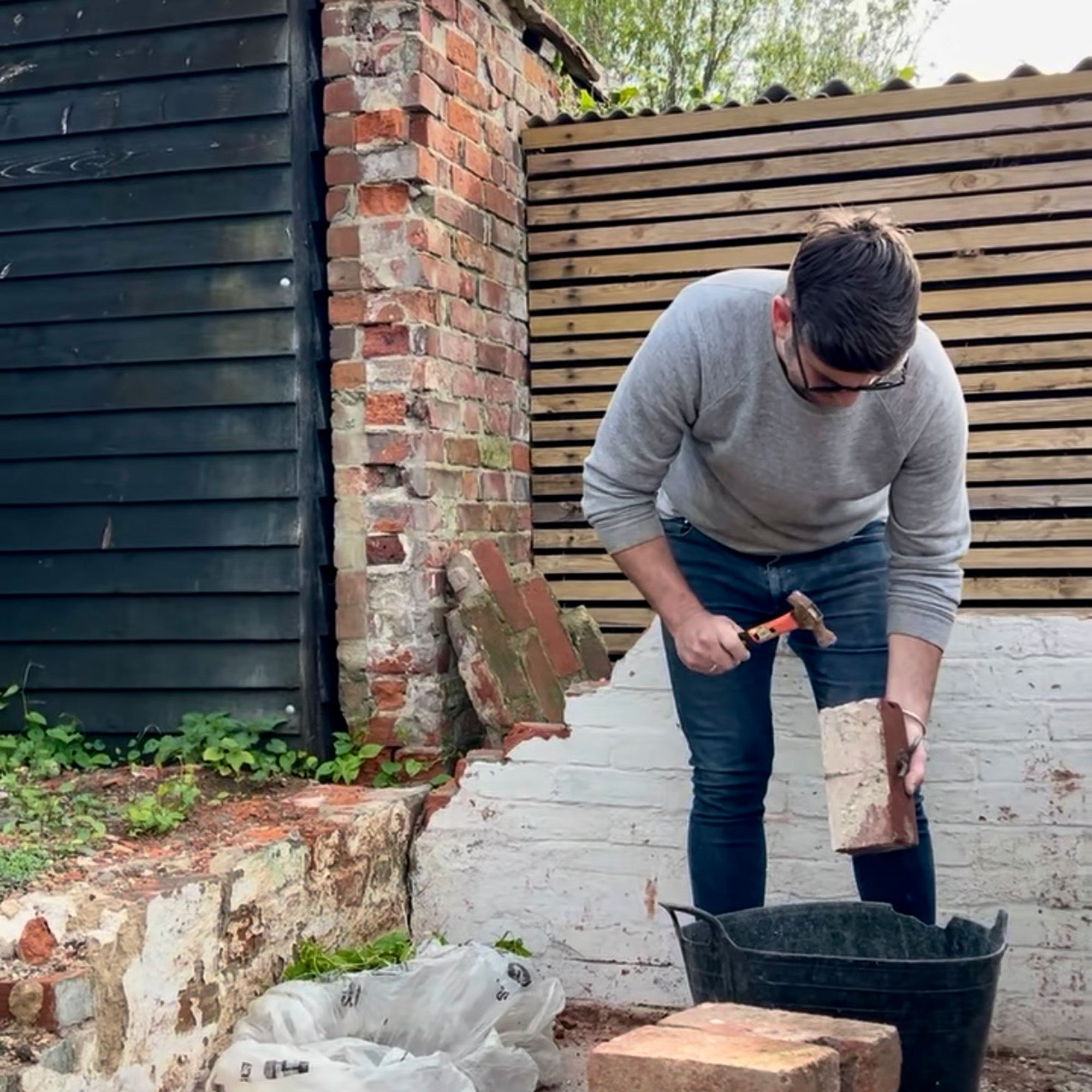 Man in garden using hammer on brick while bent over bucket