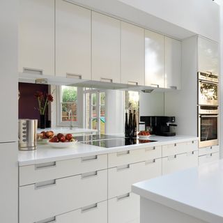 kitchen room with mirrored splashback and white cabinets