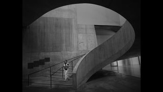 Black and white image of person walking down set of curved stairs in an industrial building