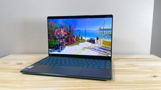 The Lenovo Yoga Slim 9i with lid open on a wood table playing an episode of Survivor