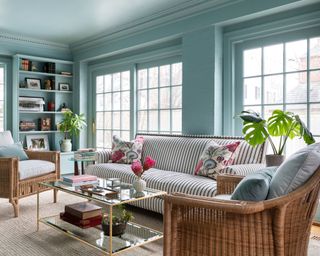 teal living room with color-drenched walls, rattan armchairs, striped sofa and fuchsia pillows