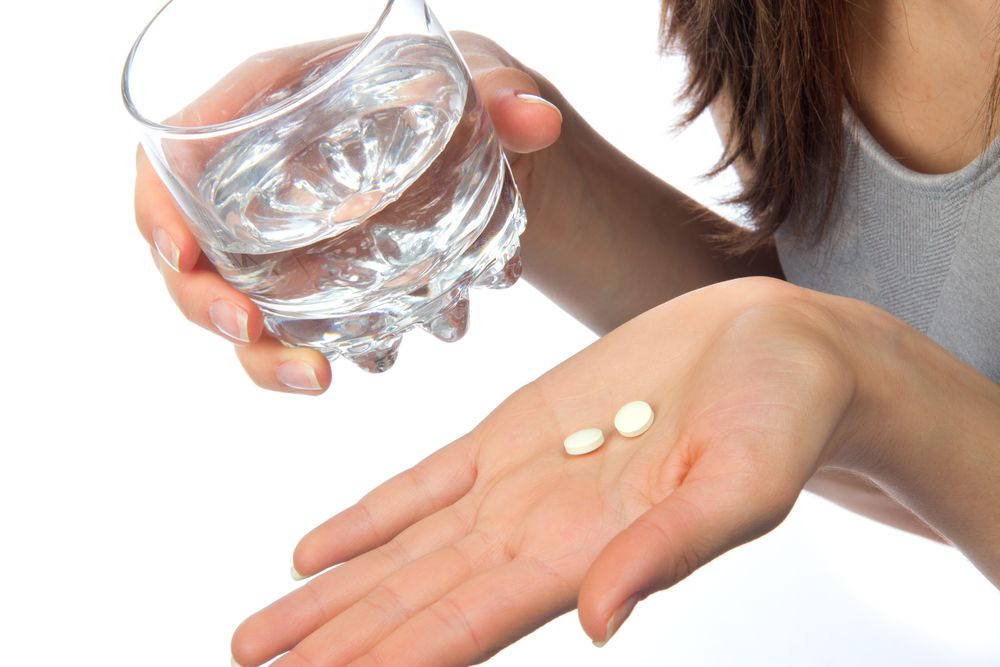 A woman holds two aspirin in her hand.