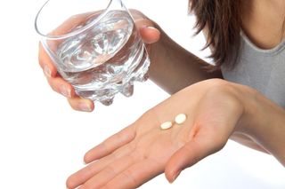 A woman holds two aspirin in her hand.