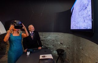 anca faur wears vr headset next to buzz aldrin. behind them is a large picture of the moon and a tv screen at upper right shows faur's virtual view of the moon