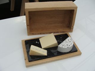 Three cheeses resting on a cheese box lid with the wooden box behind.