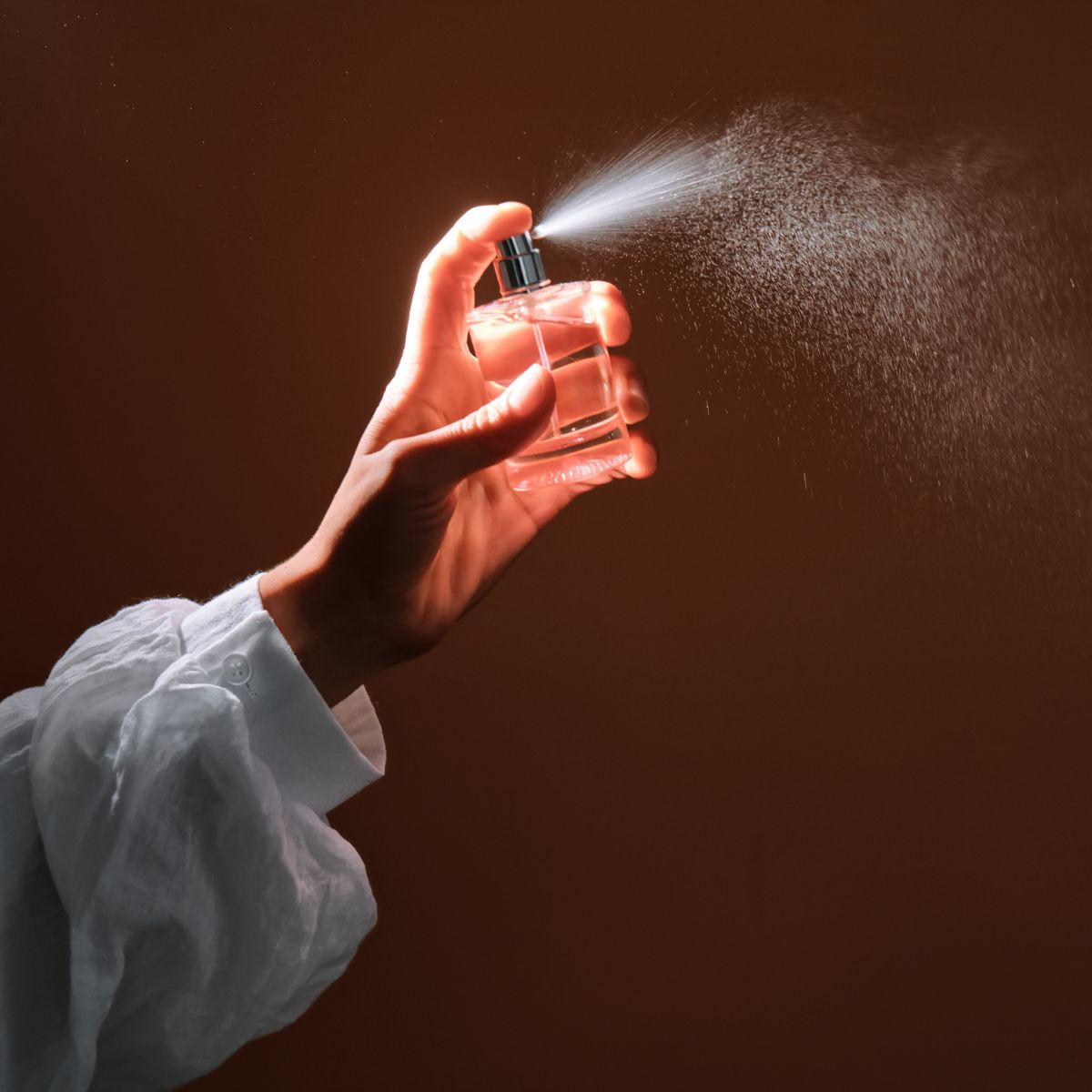 a close up of a woman&#039;s arm in a white loose-fit blouse spraying a room spray into the air