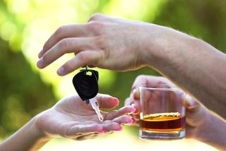 Two people exchange a set of car keys and a drink