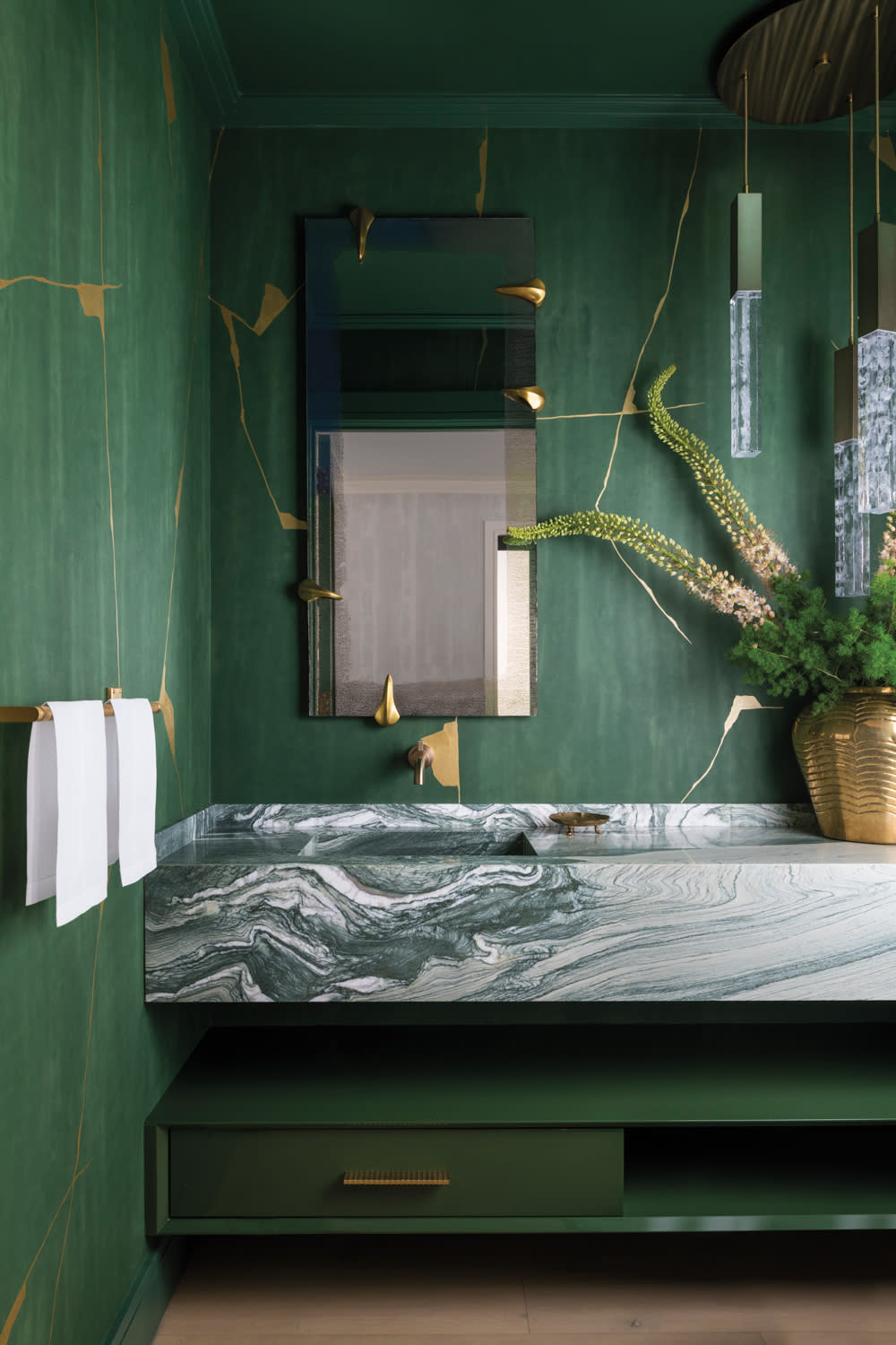 green bathroom with emerald green wallpaper, green marble vanity, vase of flowers, mirror, and towels hanging on wall